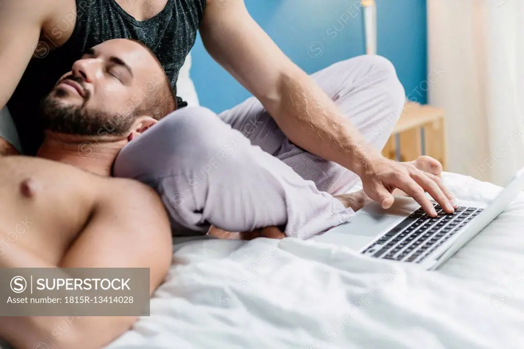 Gay couple lying in bed, using laptop