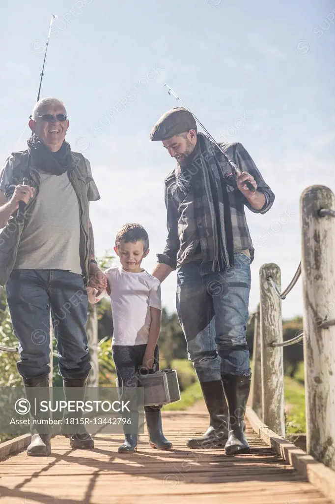 Grandfather, father and son walking over bridge with fishing equipment