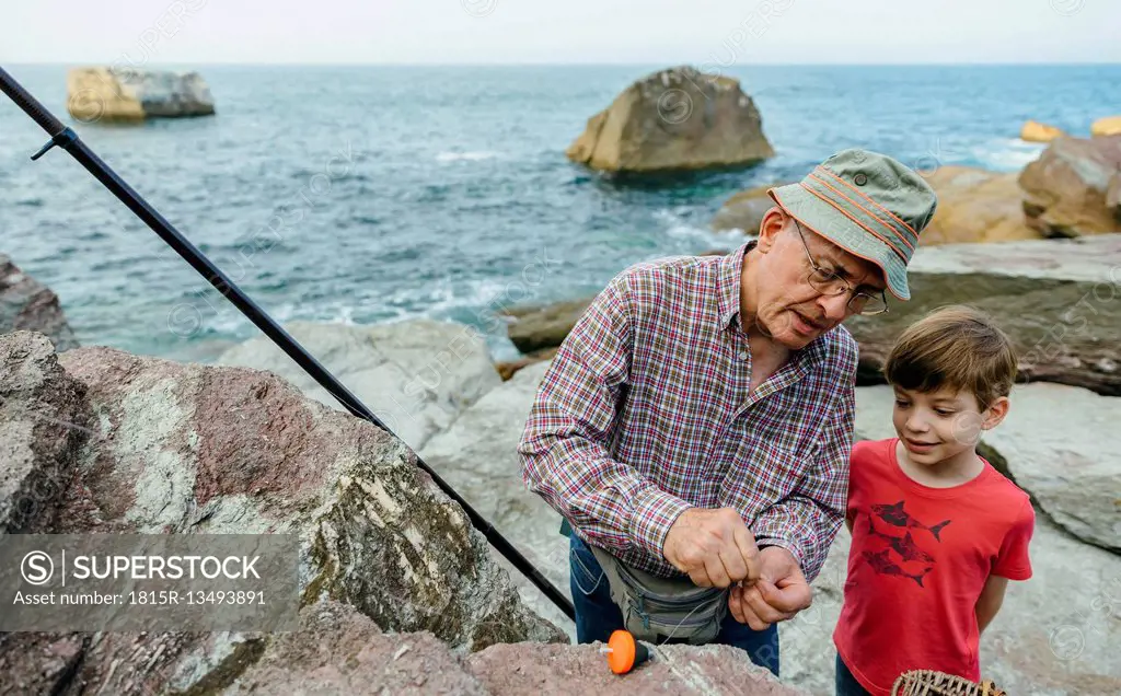 Grandfather teaching grandson fishing at the sea