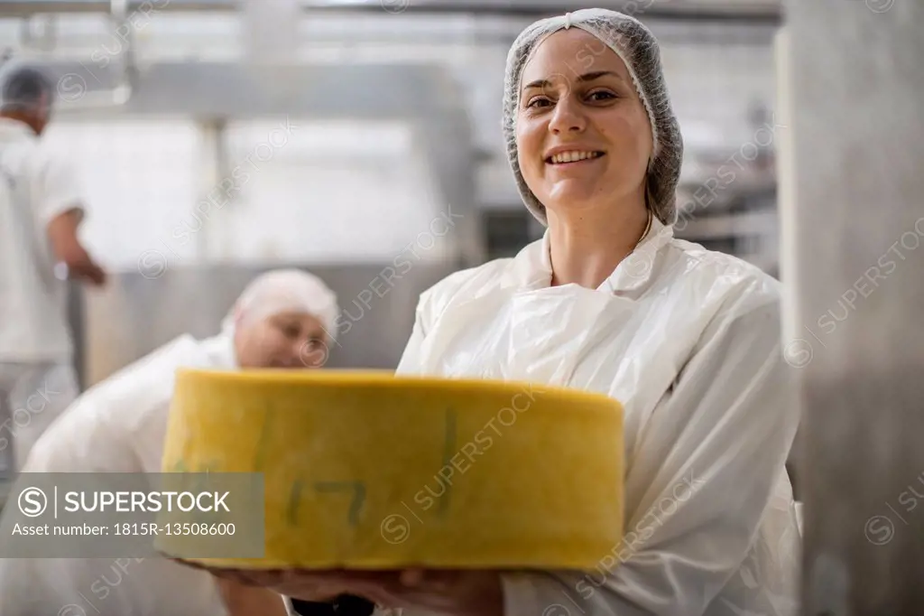 Cheese factory worker holding labeled cheese wheel