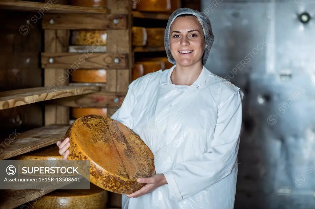 Cheese factory worker proudly holding loaf of cheese