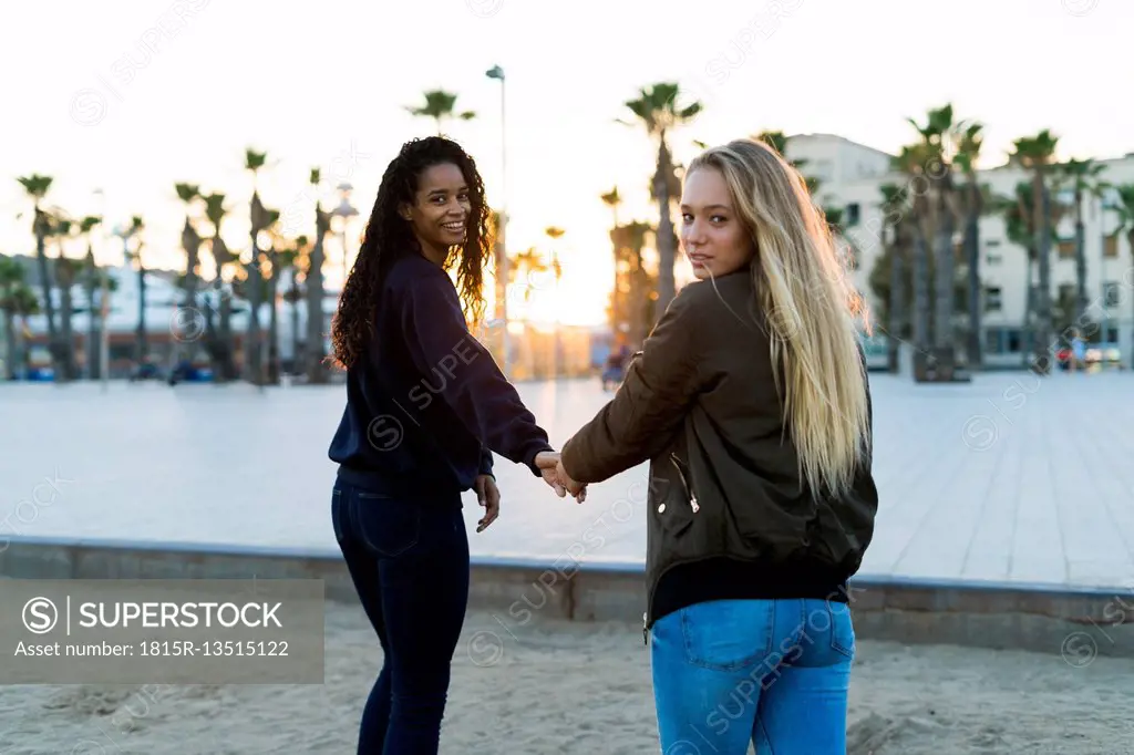 Two young women walking hand in hand at sunset