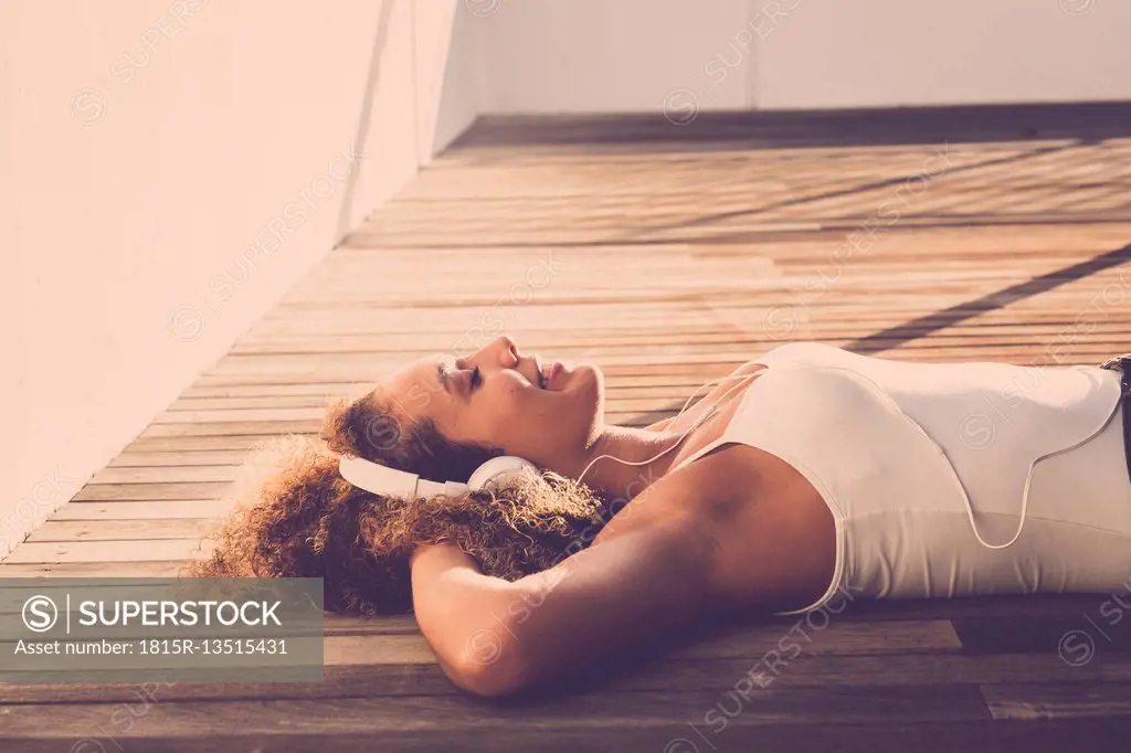 Young woman with eyes closed lying on wooden floor listening music with headphones