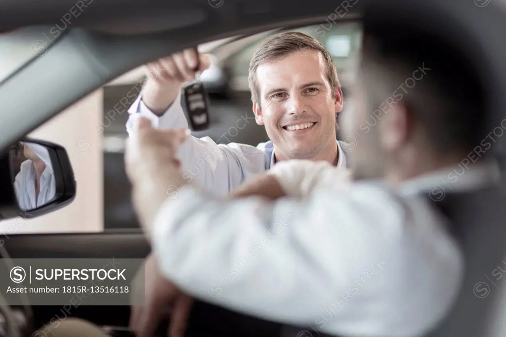 Car dealer handing over key to man at car dealership