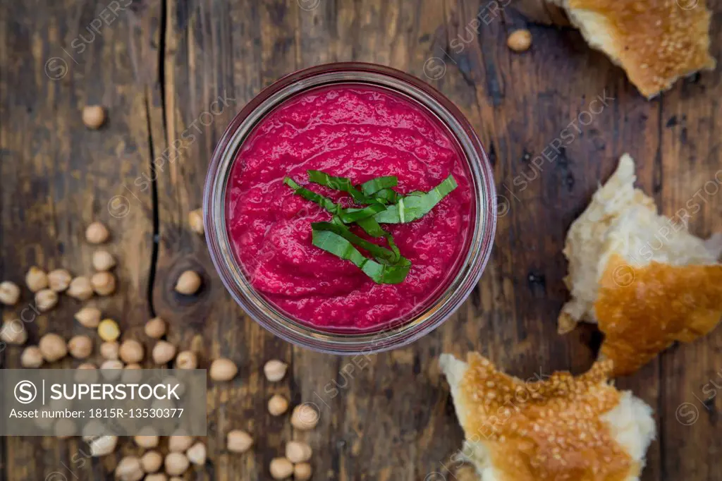 Glass of beetroot hummus, chick-peas and flat bread on dark wood