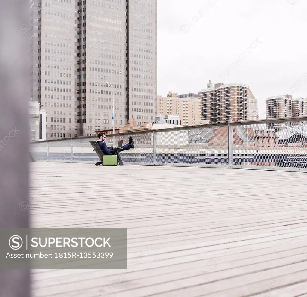 USA, New York, Manager in Manhattan sitting outdoor, using laptop