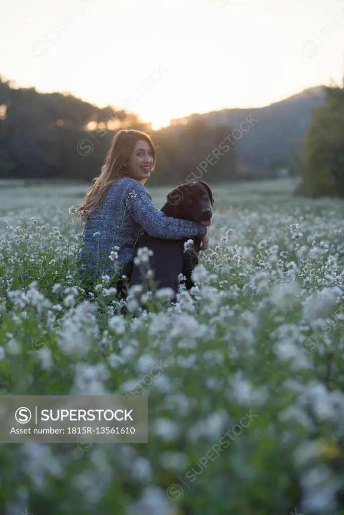 Young woman and her dog in field of flowers at twilight