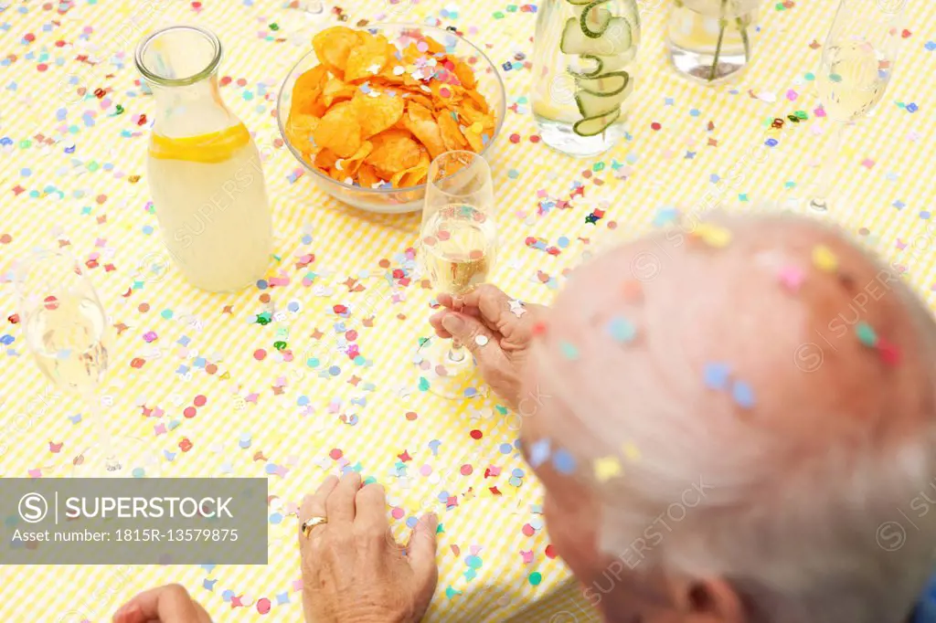 Celebrating senior sitting at table with infused water, champagne and potato chips