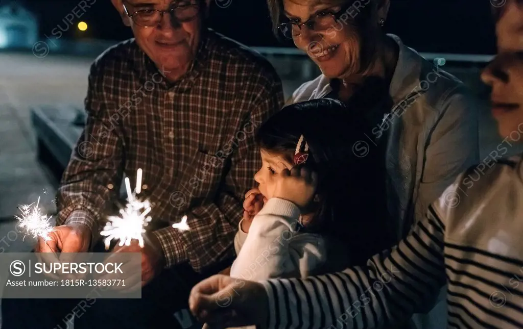 Grandparents with grandchildren holding sparklers at night