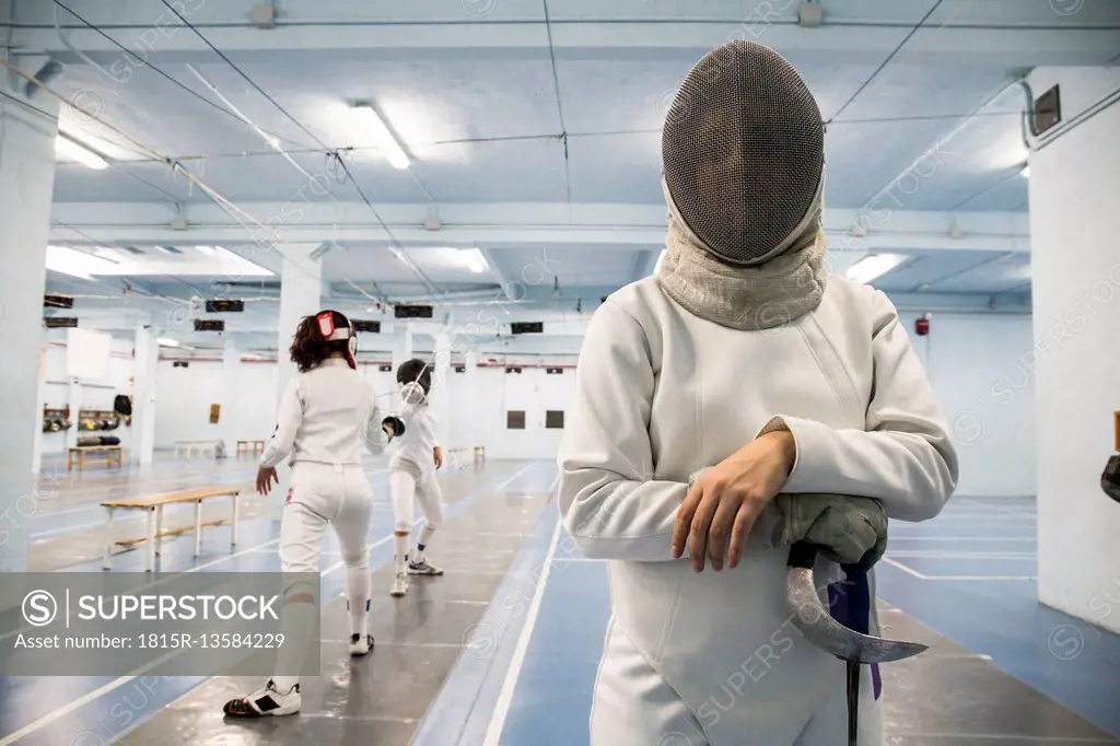 Female fencer wearing fencing mask with fencing match in the background