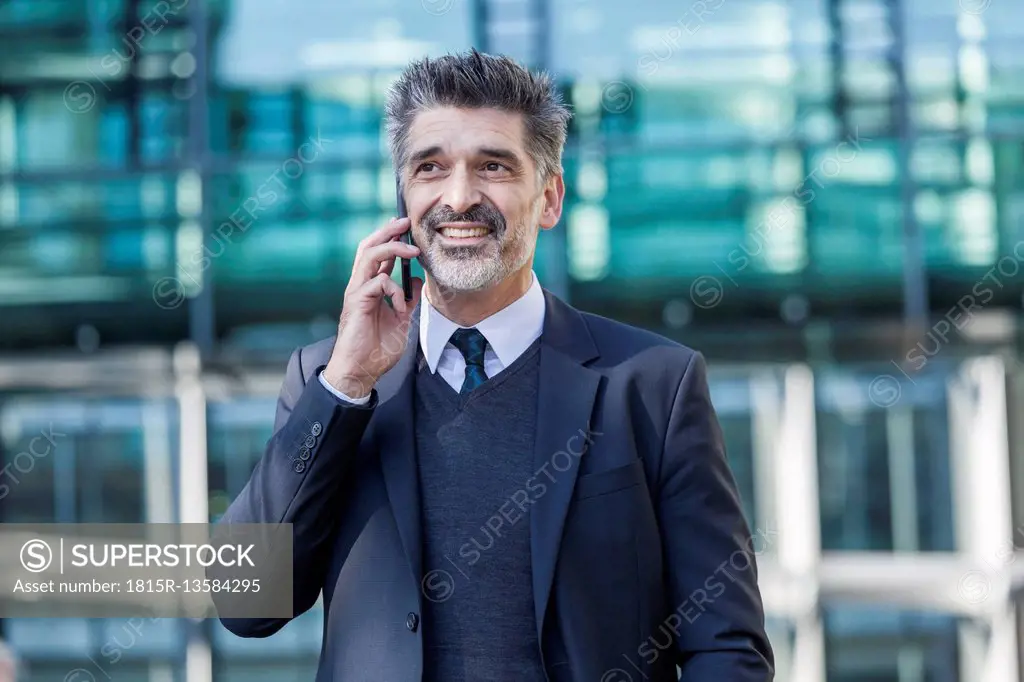 Smiling businessman outdoors on cell phone