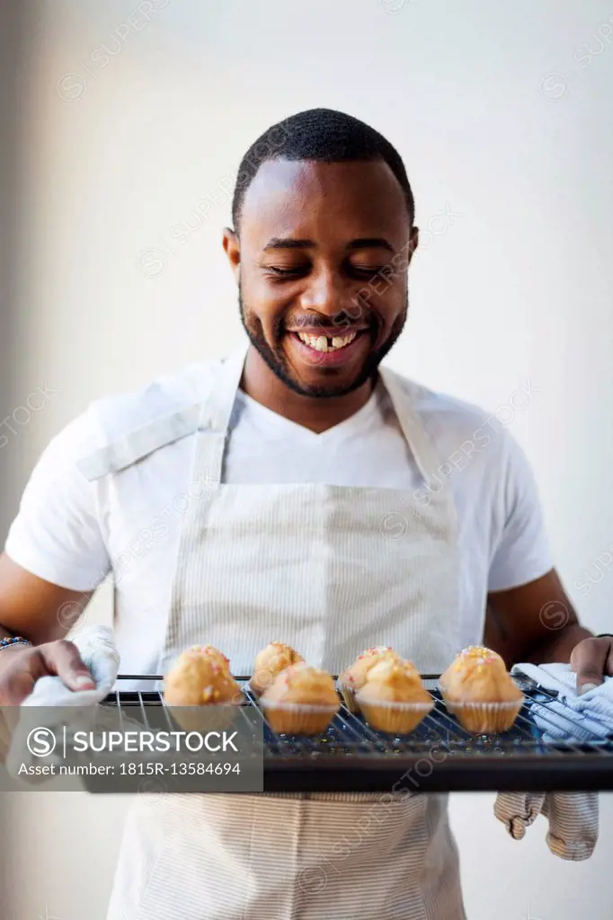 Happy young man holding tray with muffins