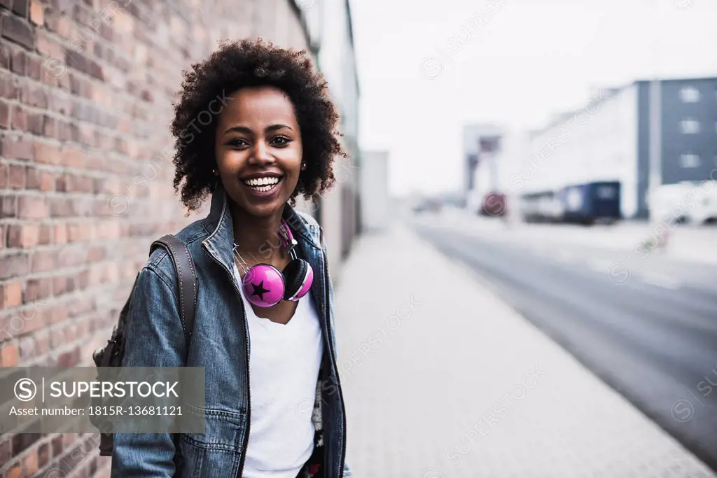 Portrait of smiling young woman with headphones and backpack standing on pavement