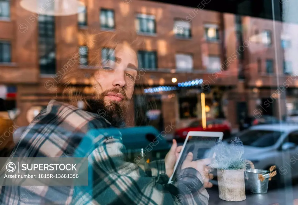 Portrait of stylish young man behind windowpane with tablet in a cafe