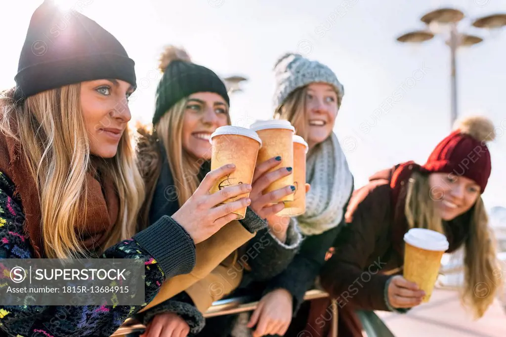 Four friends toasting with coffee to go in winter