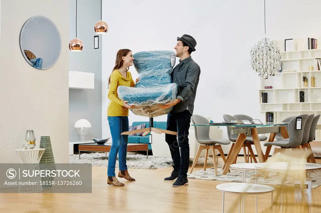 Happy couple carrying new arm chair out of furniture store