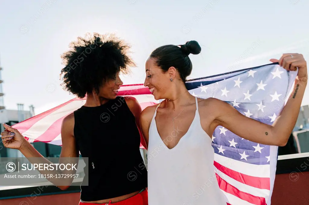 Female friends holding US American flag, standing on rooftop