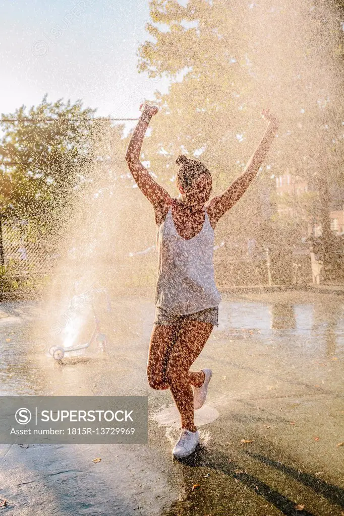 Young woman jumping water jet of a fountain