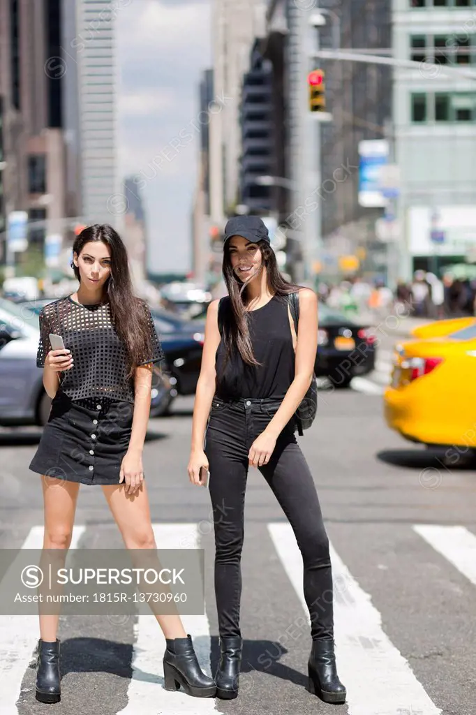 USA, New York City, two fashionable twin sisters standing on zebra crossing in Manhattan