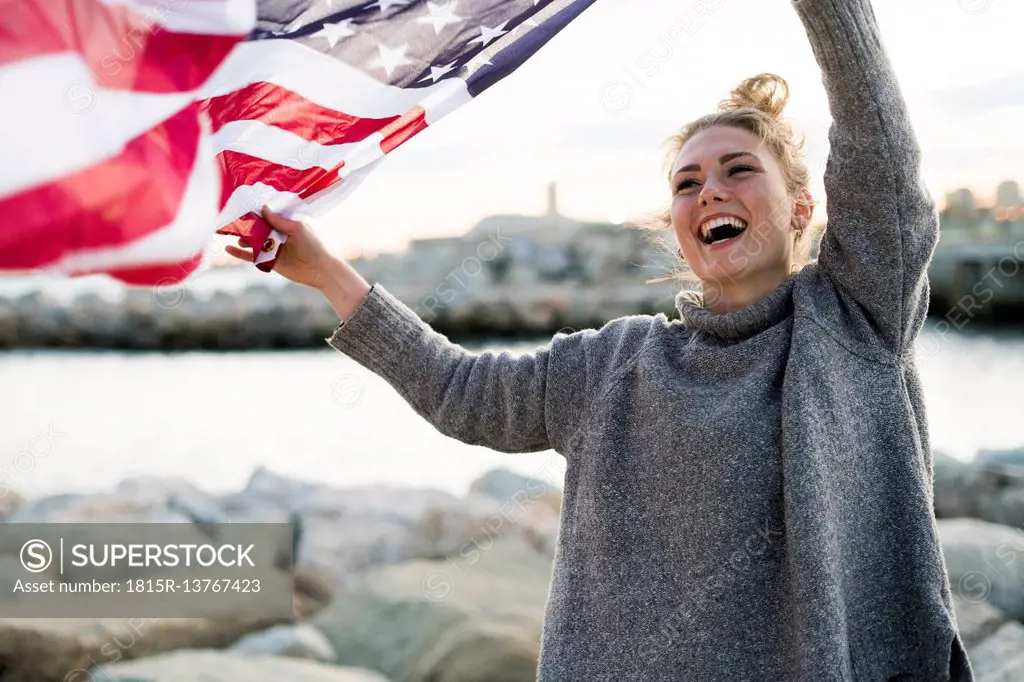 Portrait of laughing young woman holdding blowing US American flag