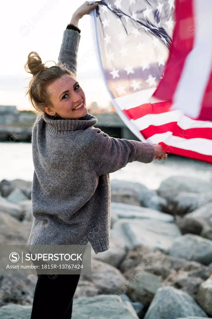 Portrait of smiling young woman holding blowing US American flag