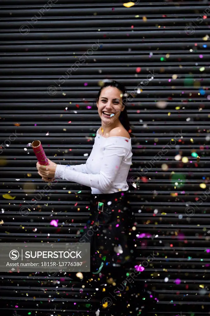Happy young woman standing in front of black roller shutter throwing confetti