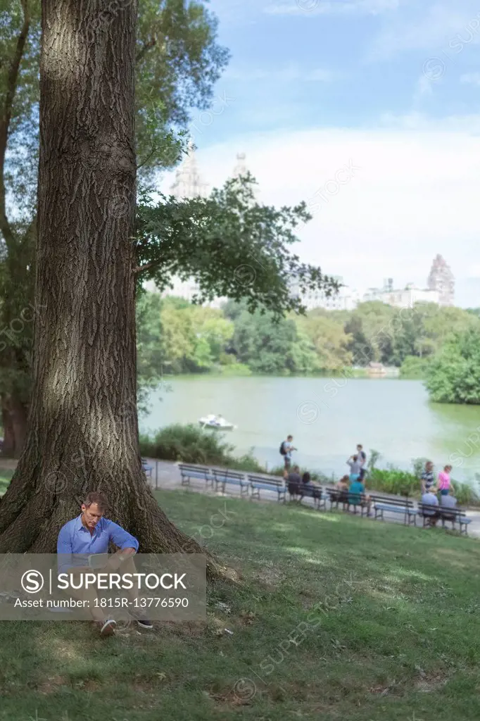 USA, Manhattan, Central Park, man with notebook sitting on a meadow in a park