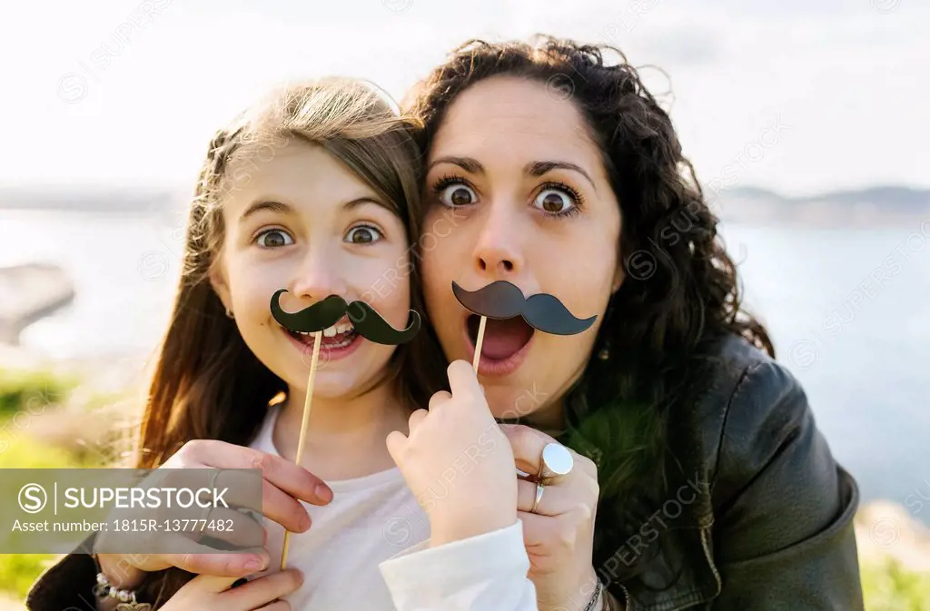 Mother and daughter having fun holding fake moustaches