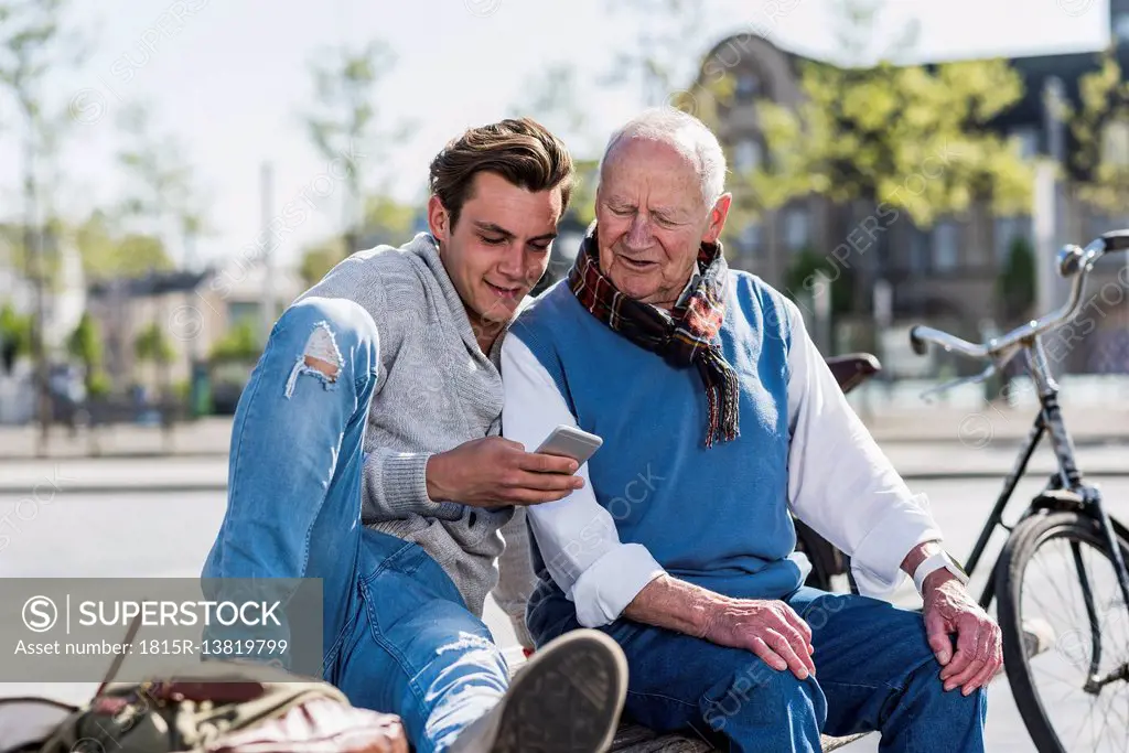 Senior man and adult grandson on a bench looking at cell phone