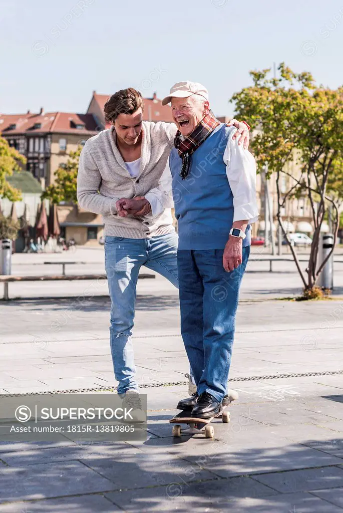 Adult grandson assisting senior man on skateboard