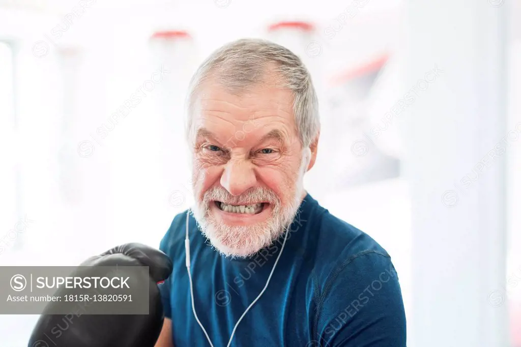 Portrait of aggressive senior man with earphones and boxing gloves in gym