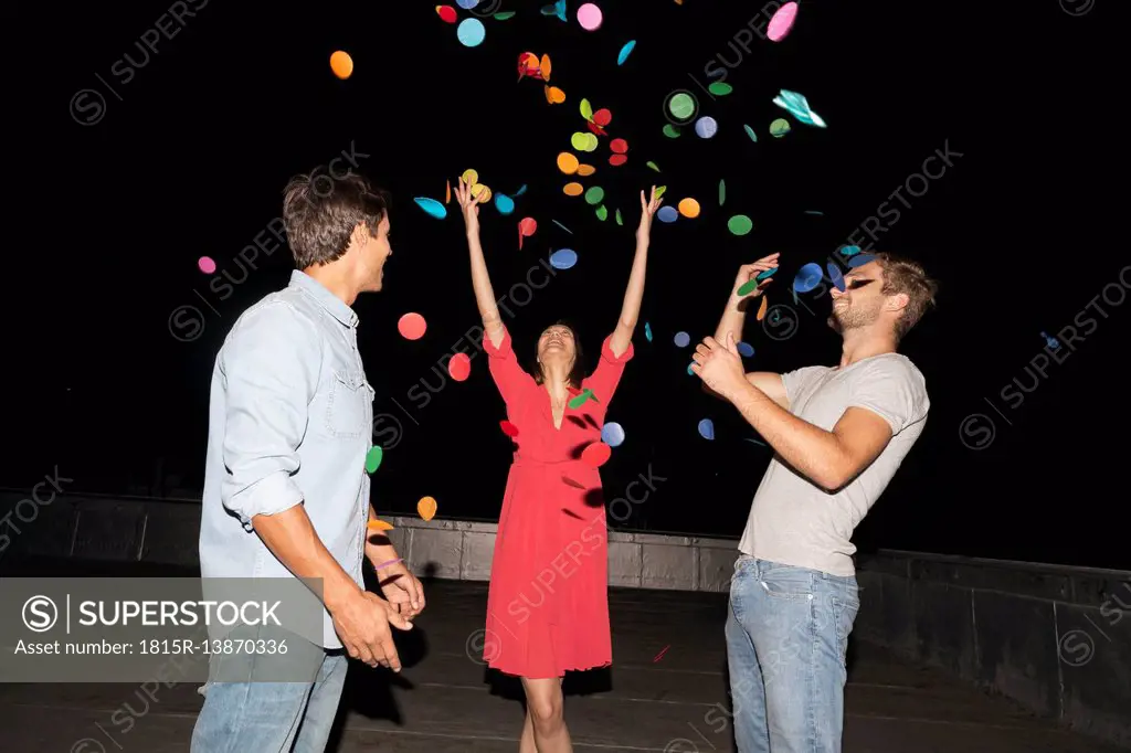 Young people having a rooftop party, throwing confetti