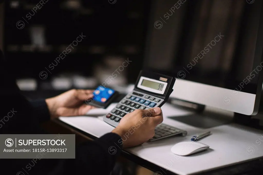 Man using calculator and credit card at desk, partial view