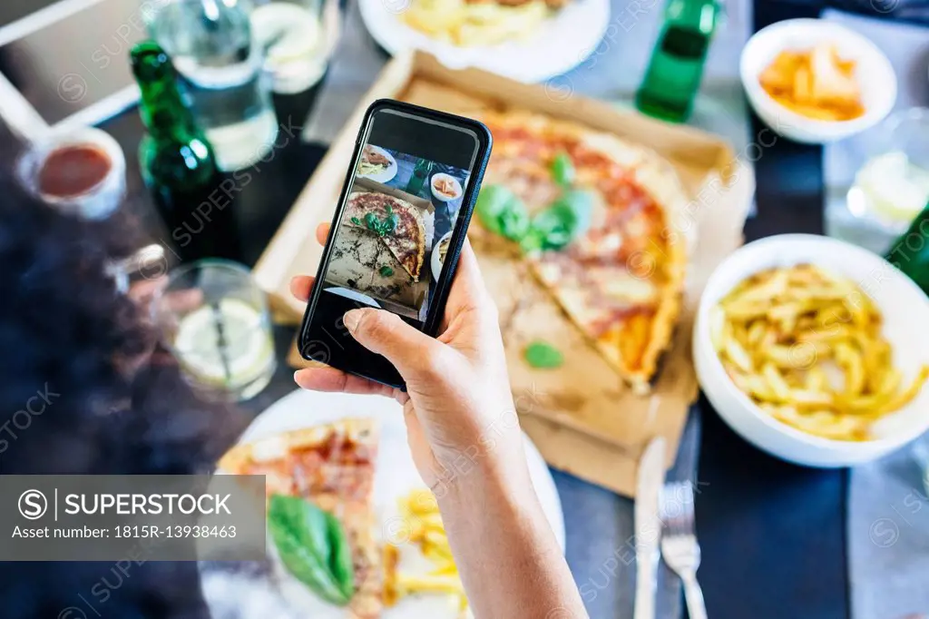 Hand taking cell phone picture of pizza on table