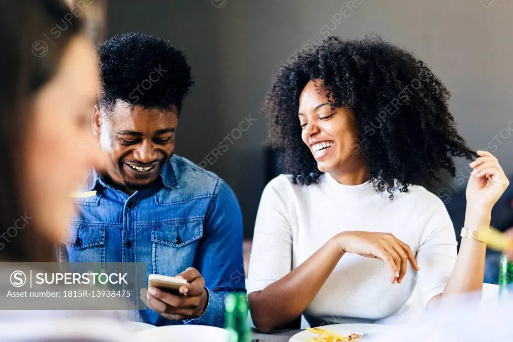 Happy couple sharing cell phone at dining table