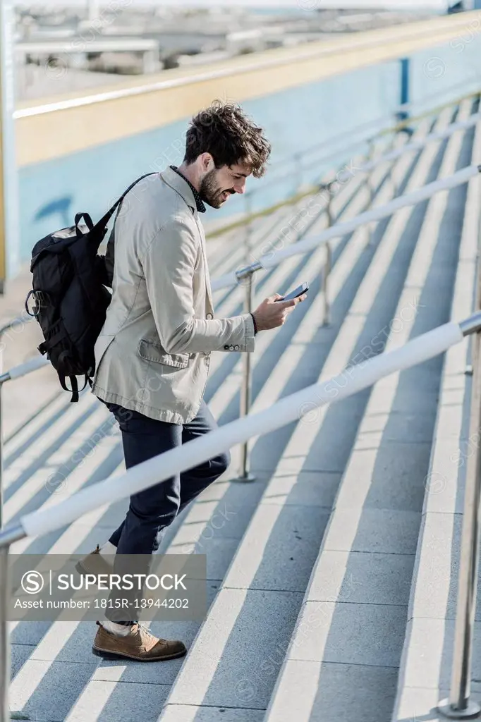 Smiling businessman walking upstairs looking at cell phone