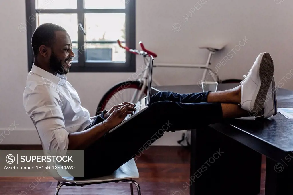 Man using laptop in home office with feet on desk