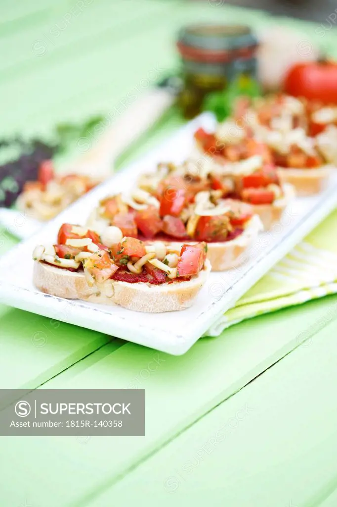 Plate of bruschetta with tomatoes, white shimeji mushrooms, herbs and olive oil on wooden table, close up