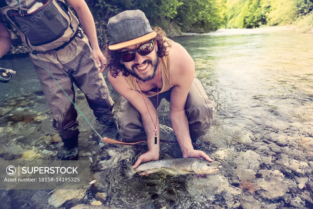 Slovenia, two men fly fishing in Soca river catching a fish