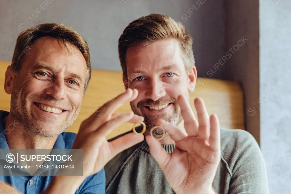 Happy gay couple holding up their wedding rings