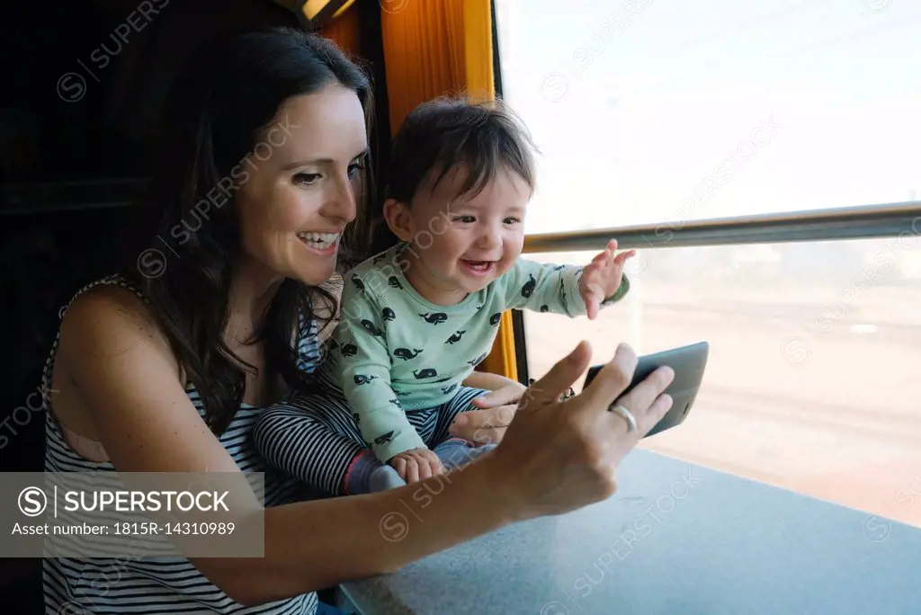 Happy mother and baby girl using smartphone while traveling by train