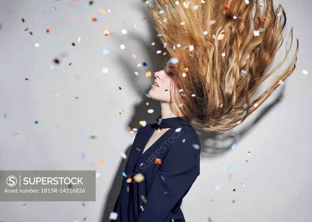 Young woman tossing hair under shower of confetti