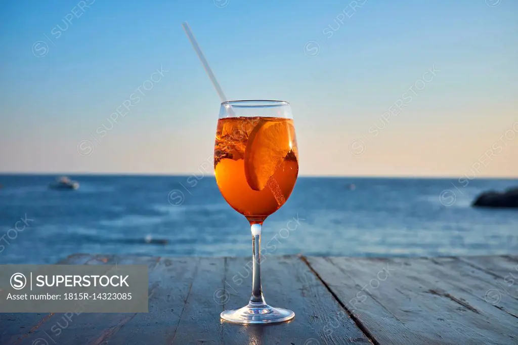 Glass of ice-cooled Spritz with orange slice in front of the sea