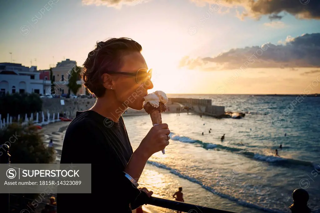 Italy, Santa Maria al Bagno, woman eating ice cream cone at backlight