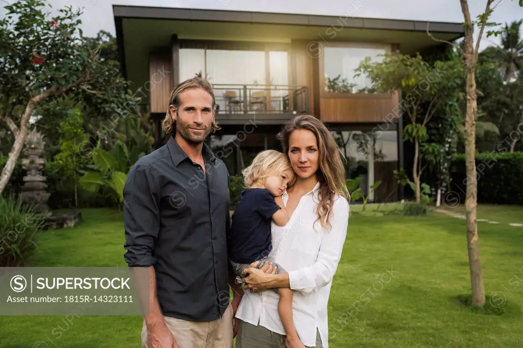 Portrait of smiling family standing in front of their design house surrounded by lush tropical garden