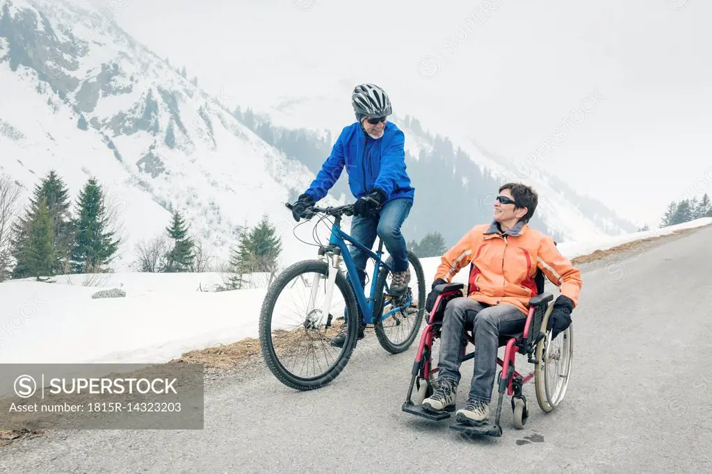 Austria, Damuels, senior couple with bike and wheelchair enjoying a winter day