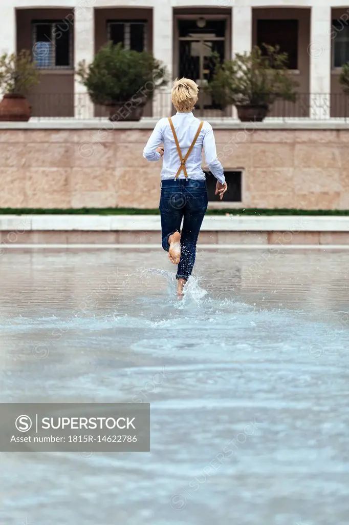 Happy teenage girl running in pool, rear view