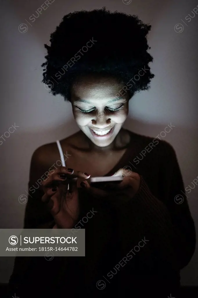 Smiling young woman using cell phone in the dark