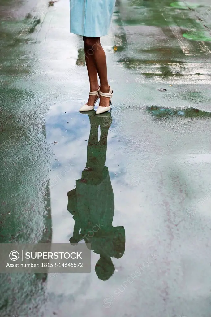 USA, New York, young african-american woman standing on street, high heels, water reflection in puddle