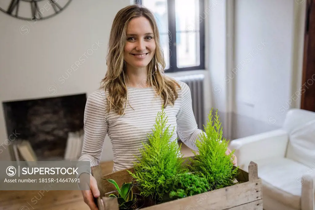 Portrait of smiling woman carrying crate with plants at home